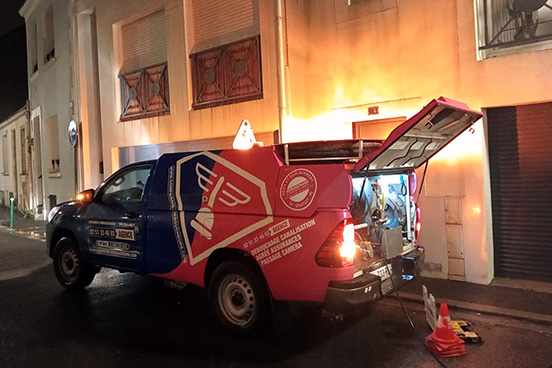 Photo d'un véhicule de pompage de la Compagnie des Déboucheurs, stationné, en intervention, de nuit devant un immeuble